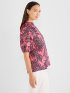 A pink relaxed-fit blouse featuring an abstract leaf print, smocked high neck, and short puff sleeves.