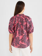 Relaxed pink botanical print blouse with smocked mock neck and gathered puff sleeves is shown from the back.
