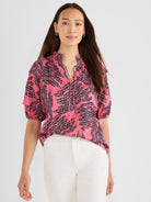 A model wears a relaxed pink blouse featuring an abstract leaf print, short puff sleeves, and a shirred split neck tie.