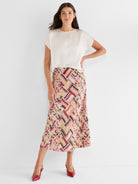 Model wears a relaxed ivory top tucked into a flowy high-waisted multicolor graphic midi skirt.