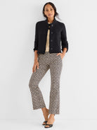 She wears a black cropped fringe jacket over fitted black and beige geometric print crop pants.