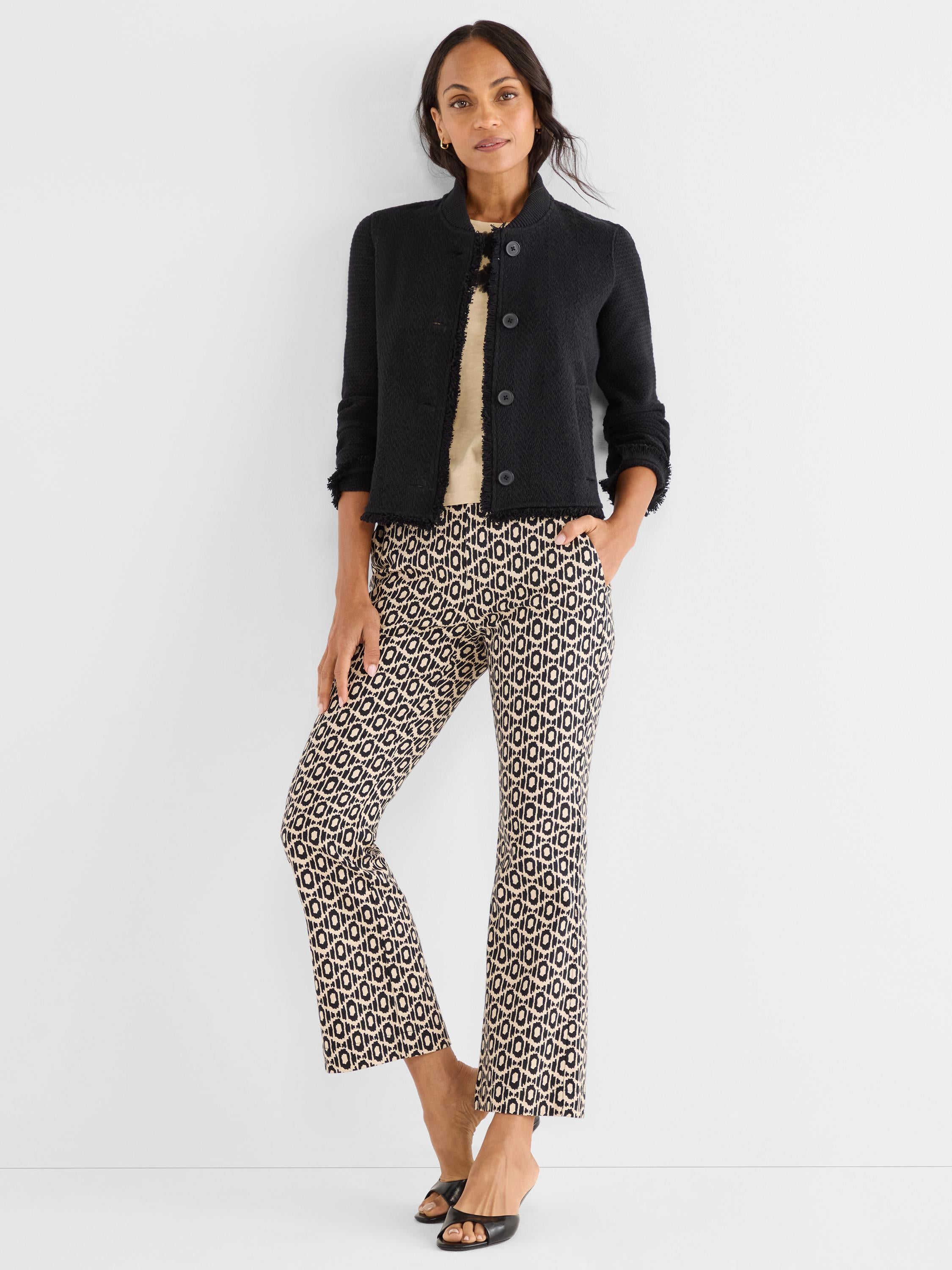 She wears a black cropped fringe jacket over fitted black and beige geometric print crop pants.