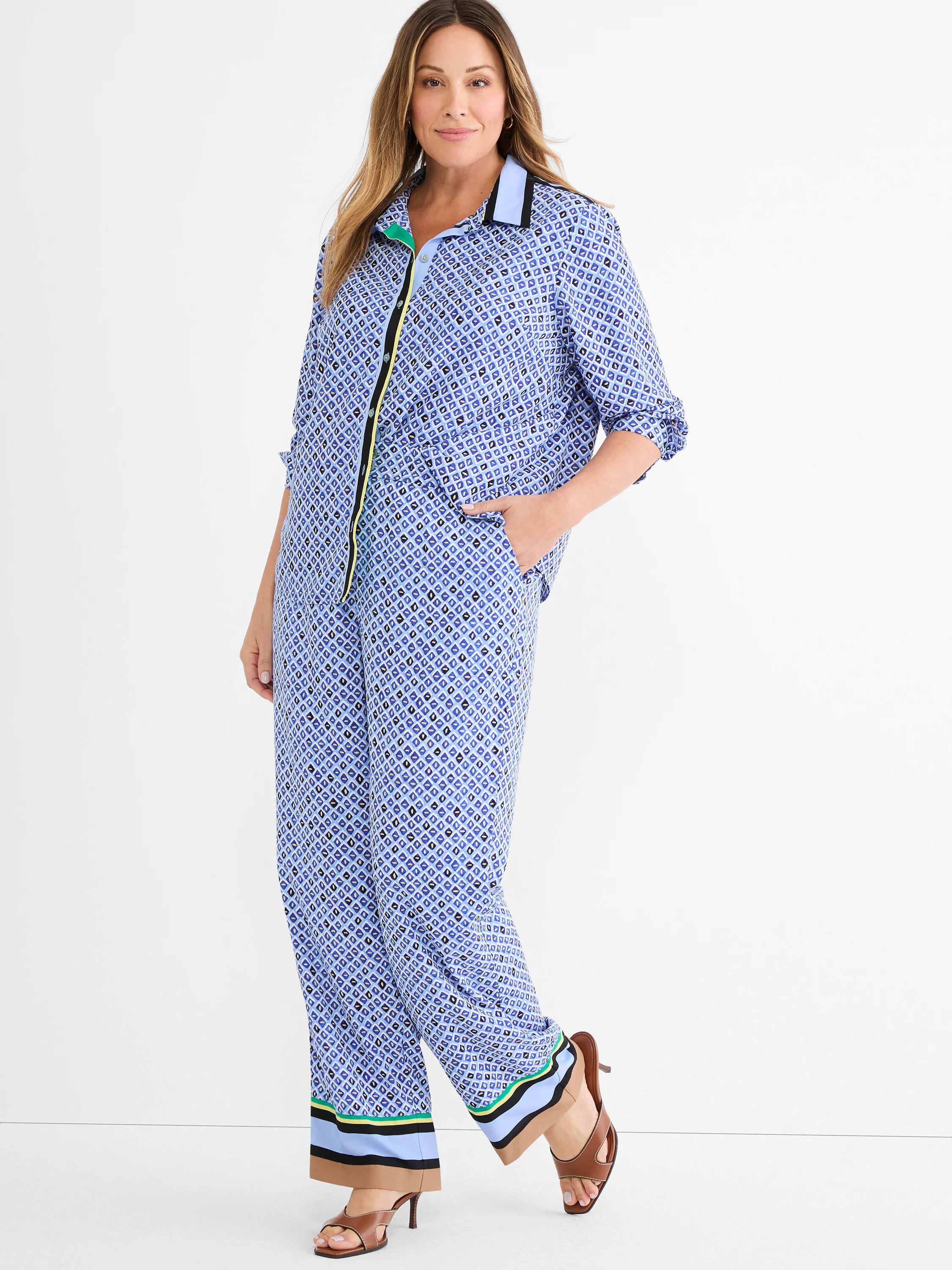 Wide-leg blue pants with a mosaic pattern of geometric shapes. Cuffs have striped trim in tan, black, light blue, and...