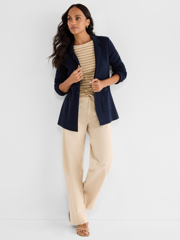 A relaxed navy knit blazer features lapels and large patch pockets, paired with wide-leg beige trousers.