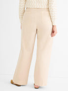 Relaxed fit beige wide-leg trousers are detailed from the back, showing a high waist and simple flat pockets.