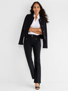 A model wears a black textured jacket with fringe trim and high-waisted black pants detailed with gold buttons.