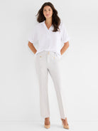 A loose white collared short-sleeve shirt is paired with high-waisted tailored light gray ankle pants accented with gold.