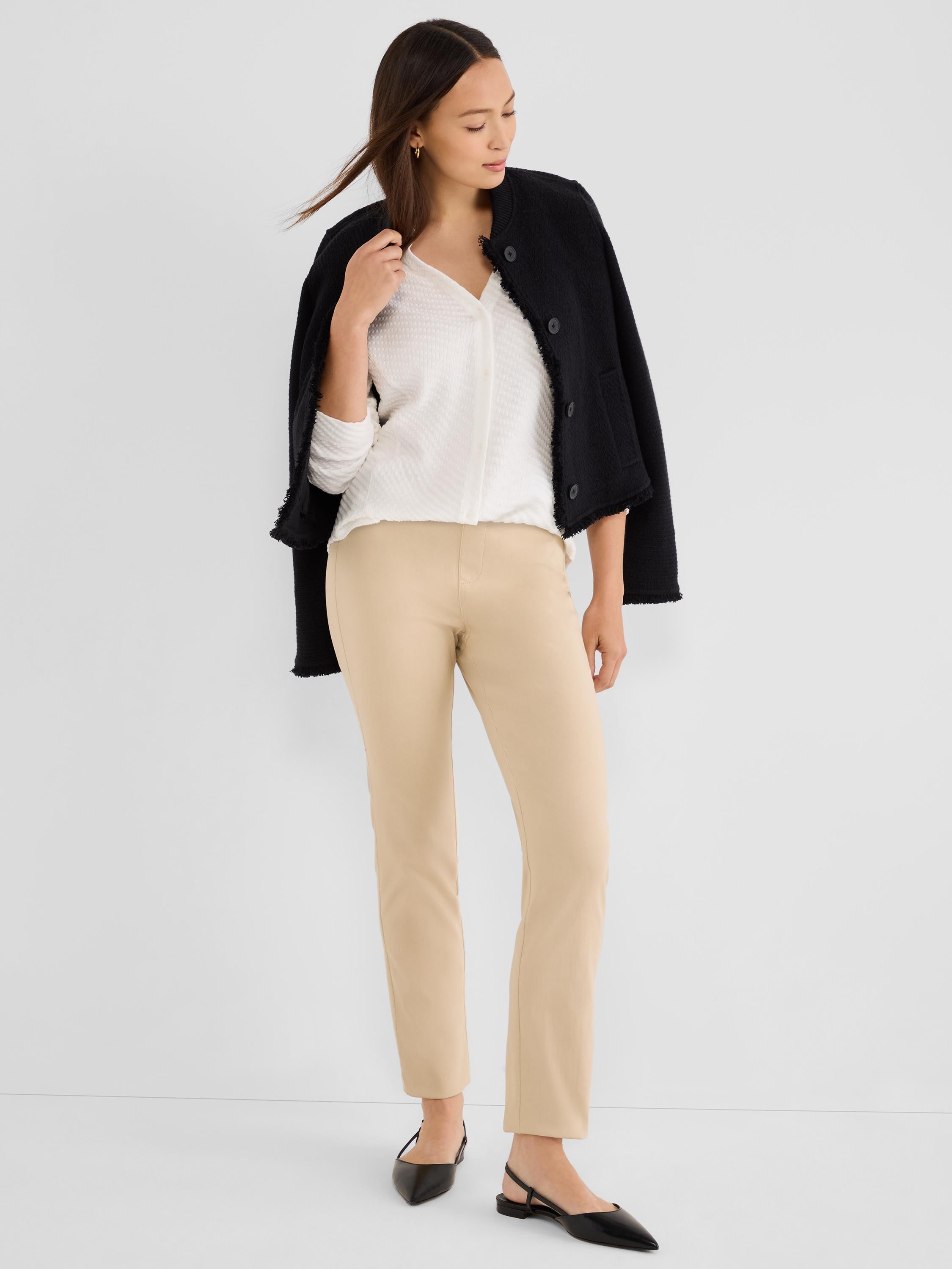 Slim beige ankle pants are paired with a textured white top and a collarless black tweed jacket draped over the shoulders.