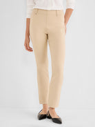 These beige high-rise slim ankle pants feature a clean pull-on waistband detailed with small metal studs.