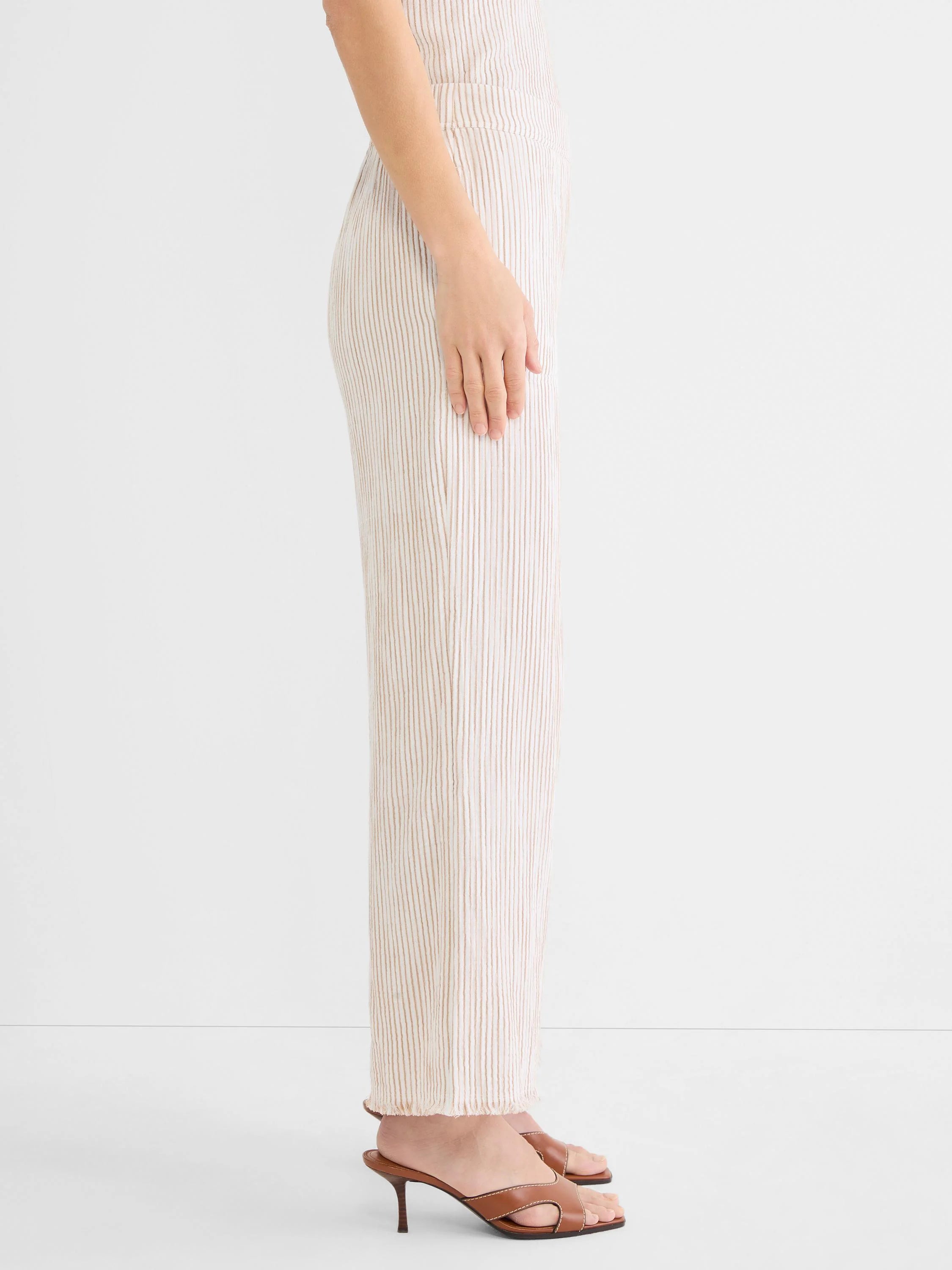 Cream wide-leg gauze pants with brown vertical pinstripes and a frayed hem. Model wearing.