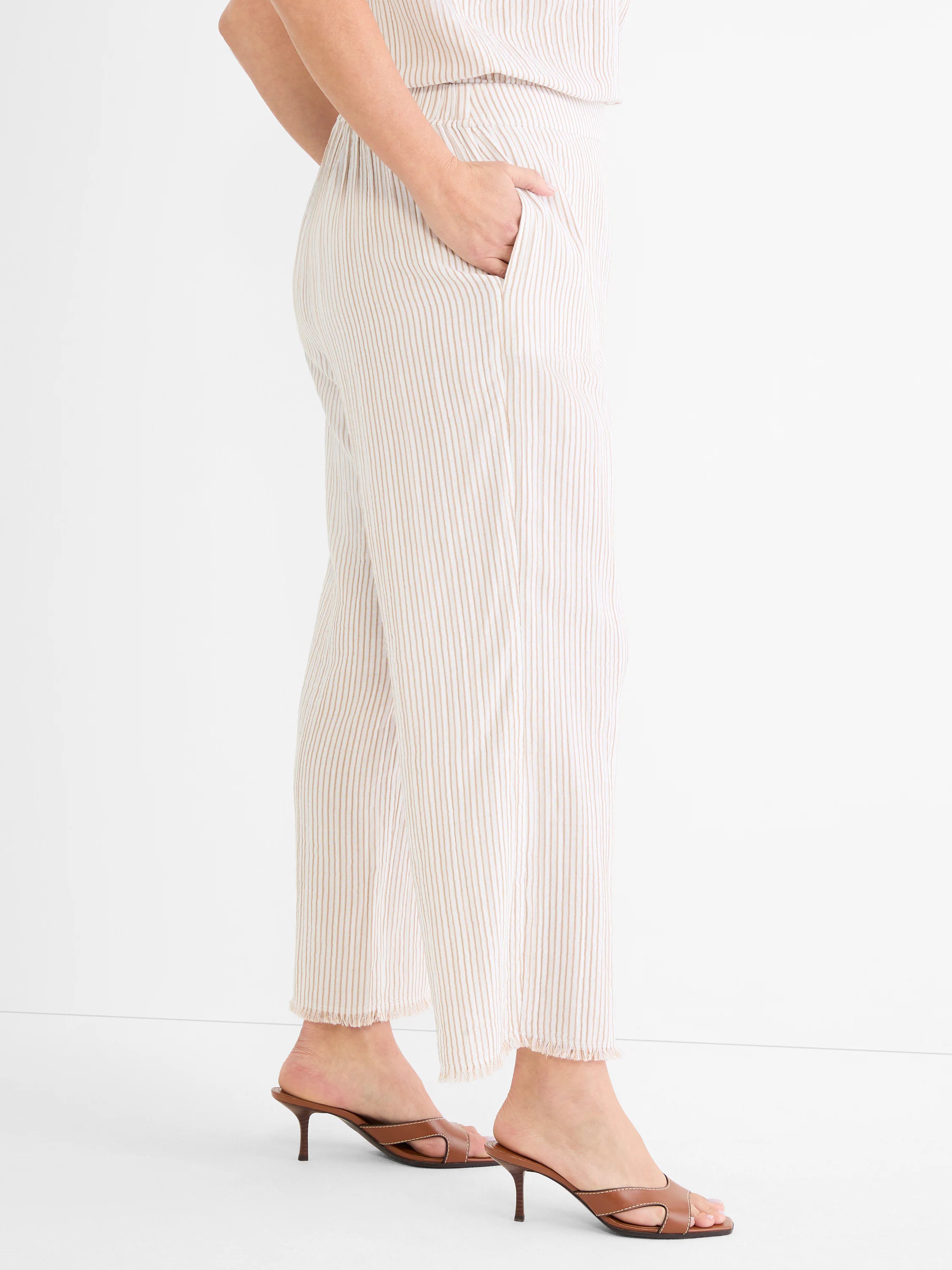 Ecru wide-leg pants with thin brown pinstripes. Features elastic waist, side pocket, and frayed hem.