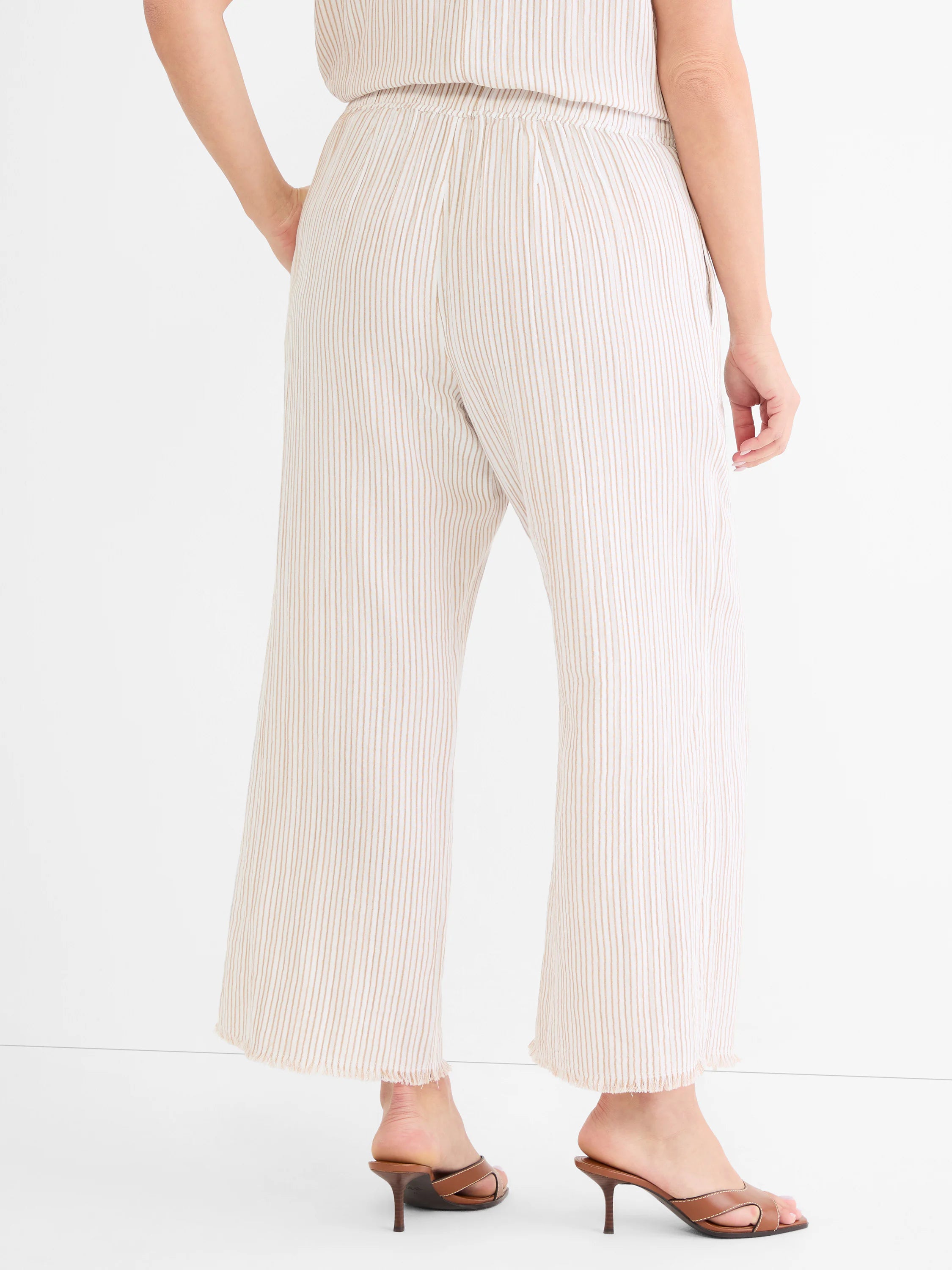 Cream wide-leg gauze pants with thin tan pinstripes, an elastic waist, and frayed hems, shown from behind.