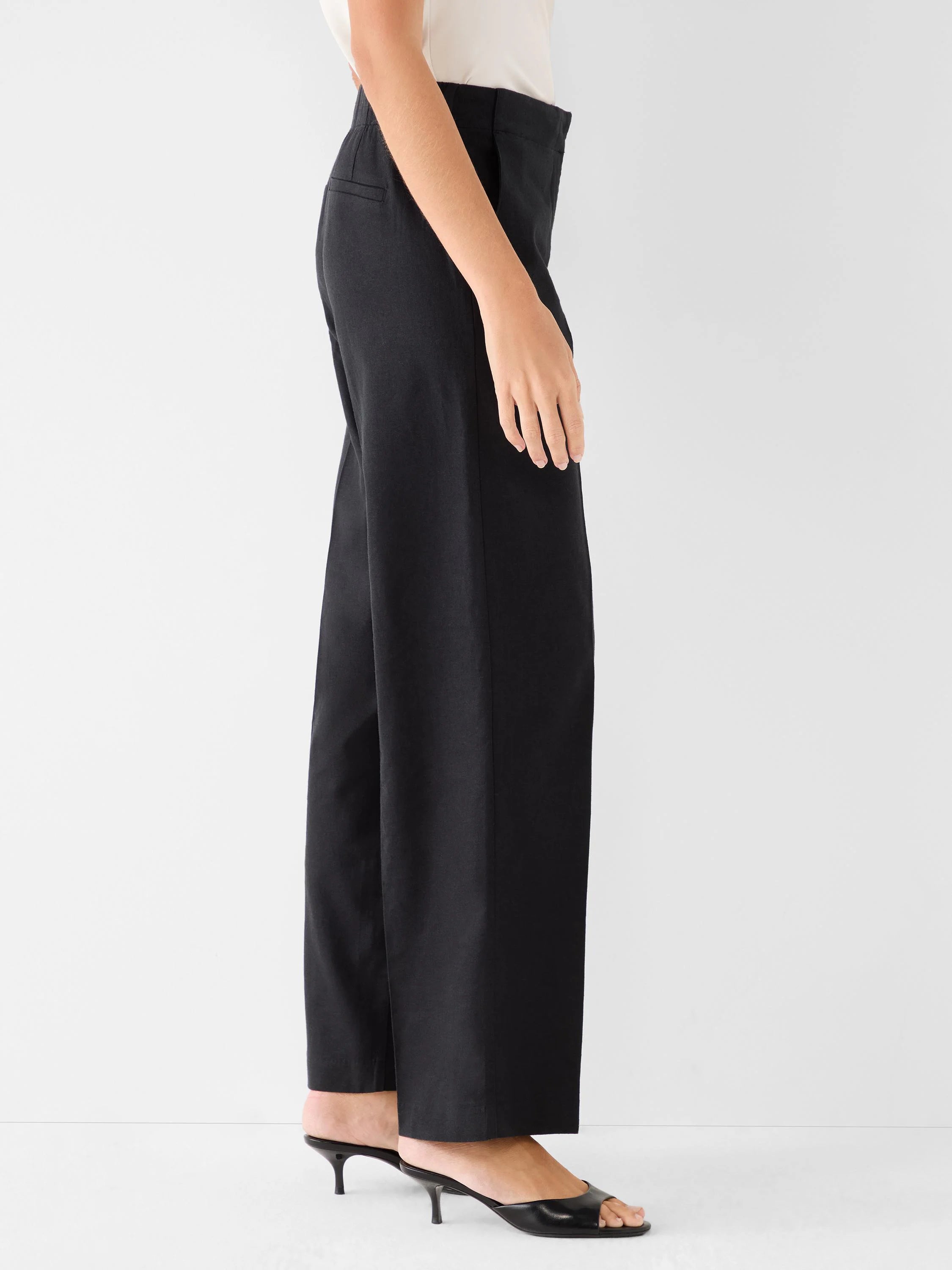 Black wide-leg linen pants on a model, seen from the side. High-waisted, relaxed fit, ankle length.