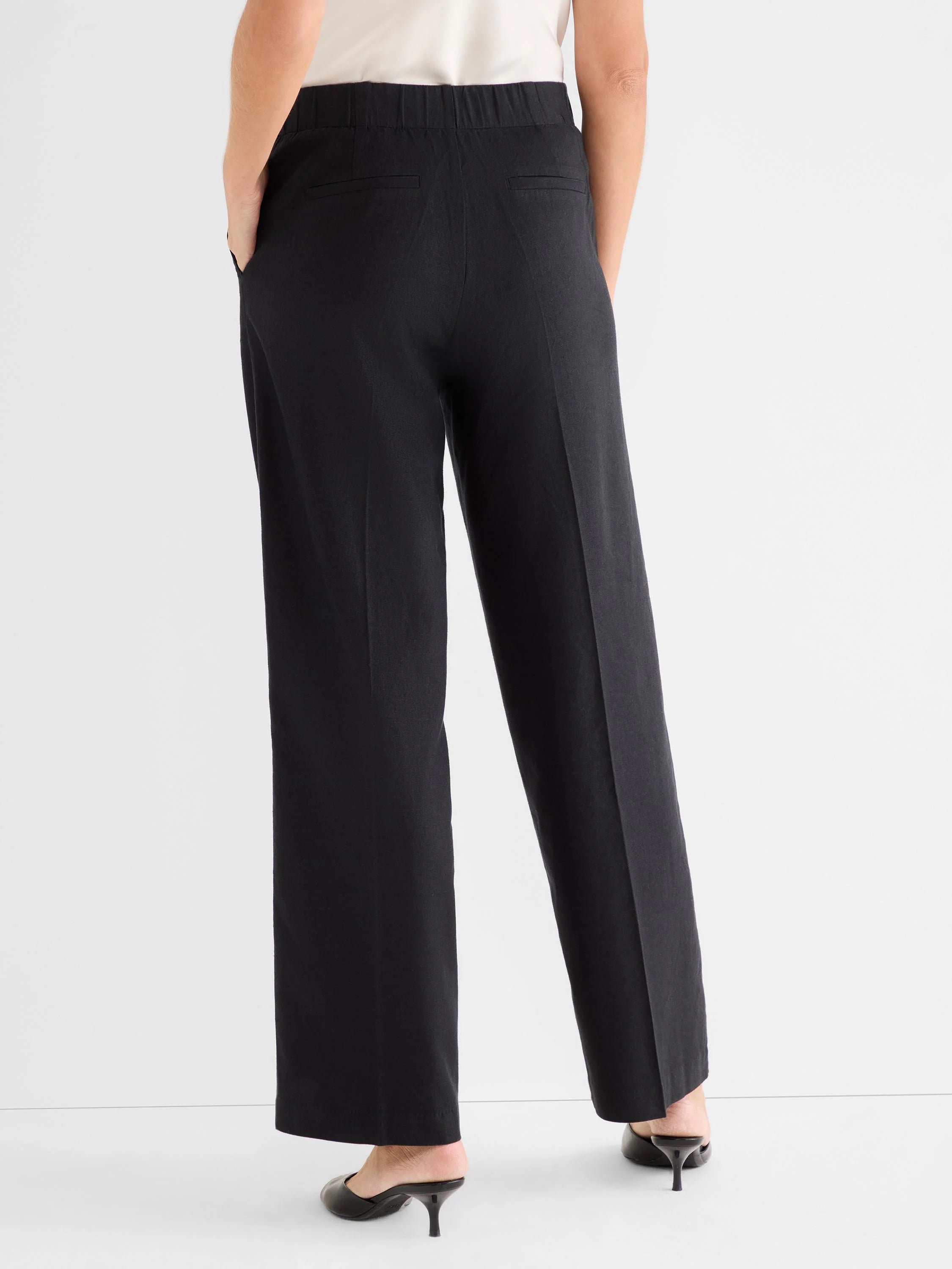 Black wide-leg pants, seen from behind on a model. Features an elasticized back waist and two back welt pockets.