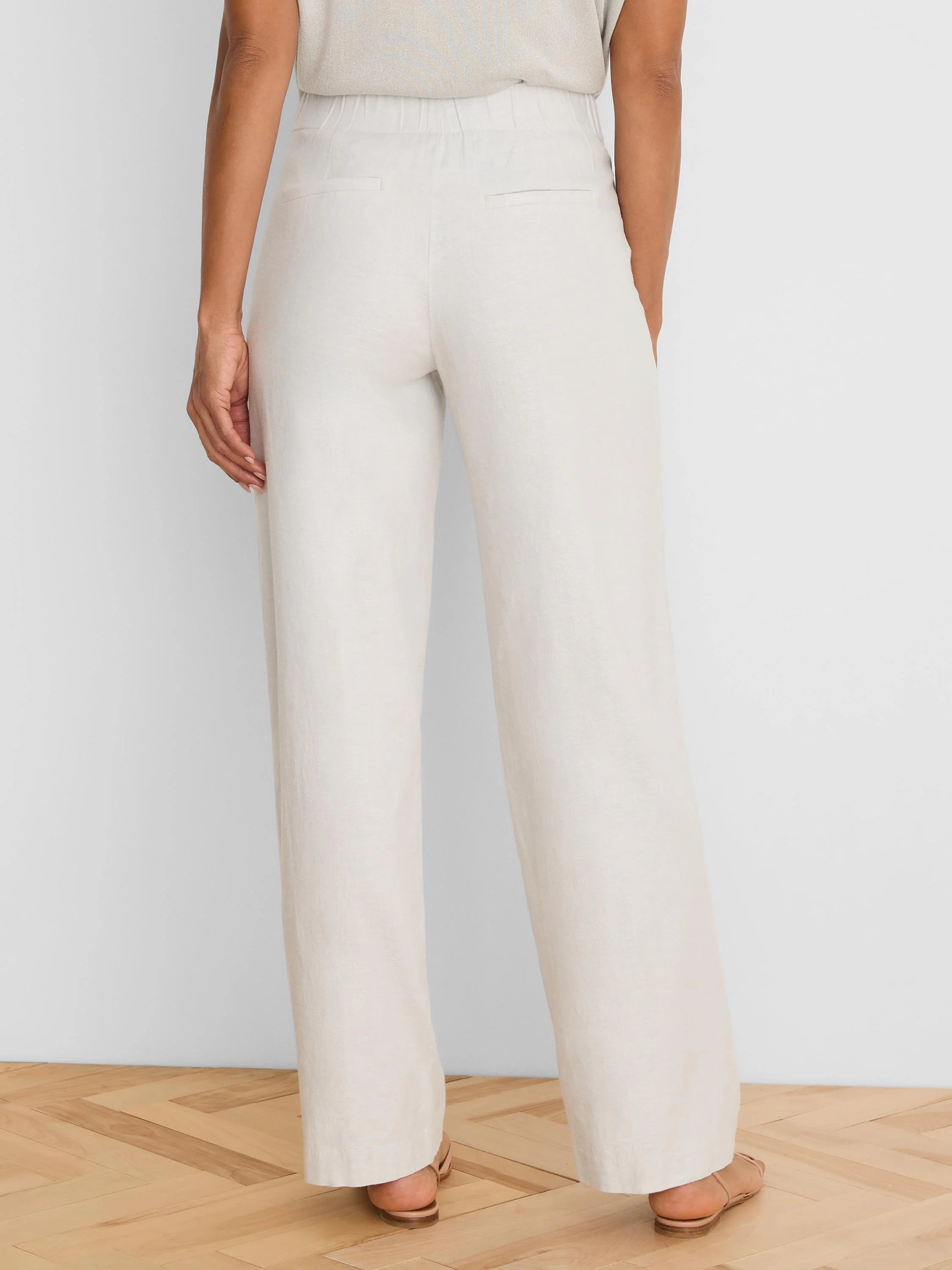 Cream wide-leg linen pants with an elasticized back waist and two back welt pockets, shown from behind.