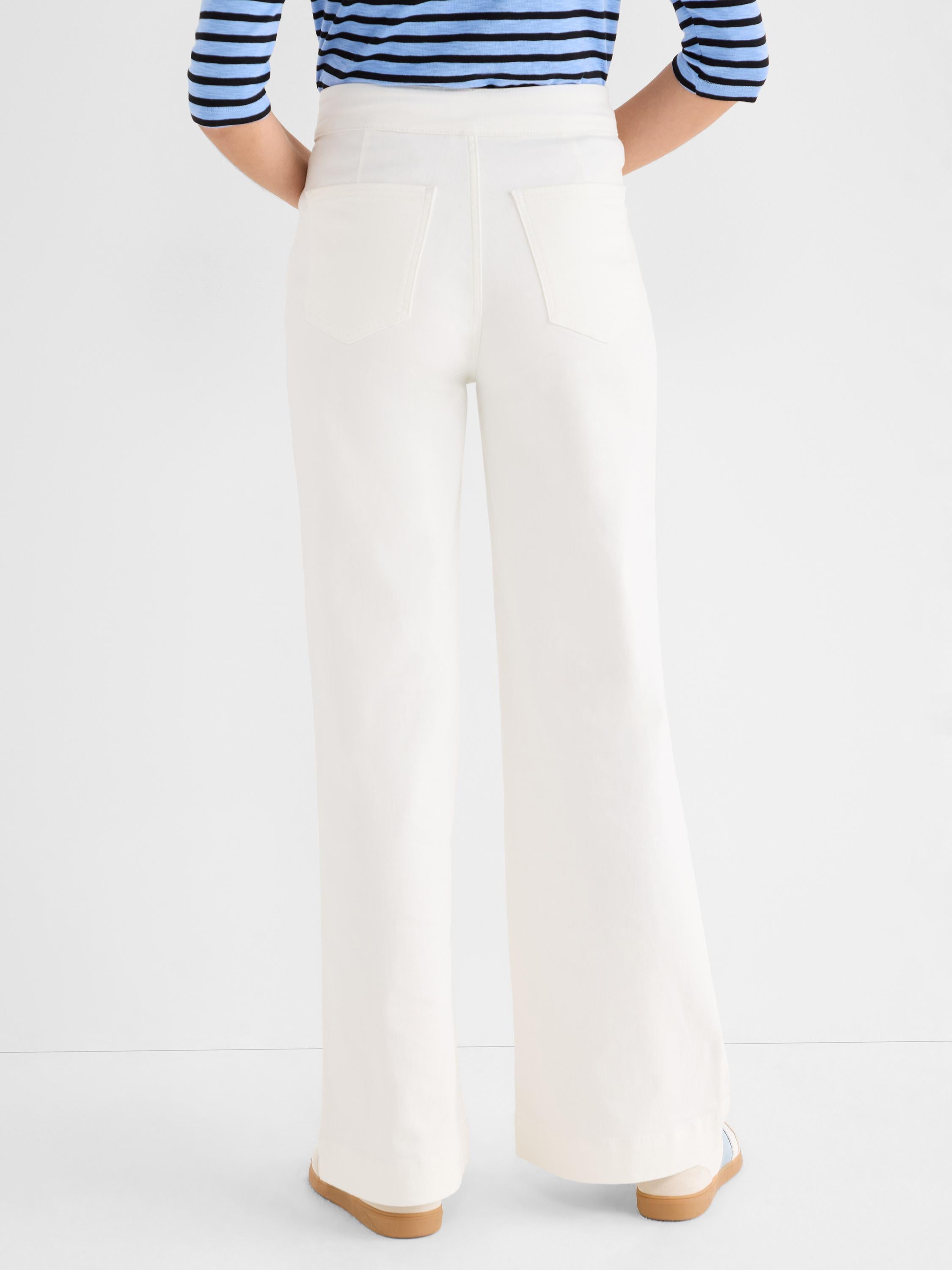 Ivory wide-leg high-waisted pants featuring patch back pockets are worn by the model.