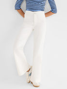 Model wears high-waisted, white wide-leg trousers with a clean front and single button closure.