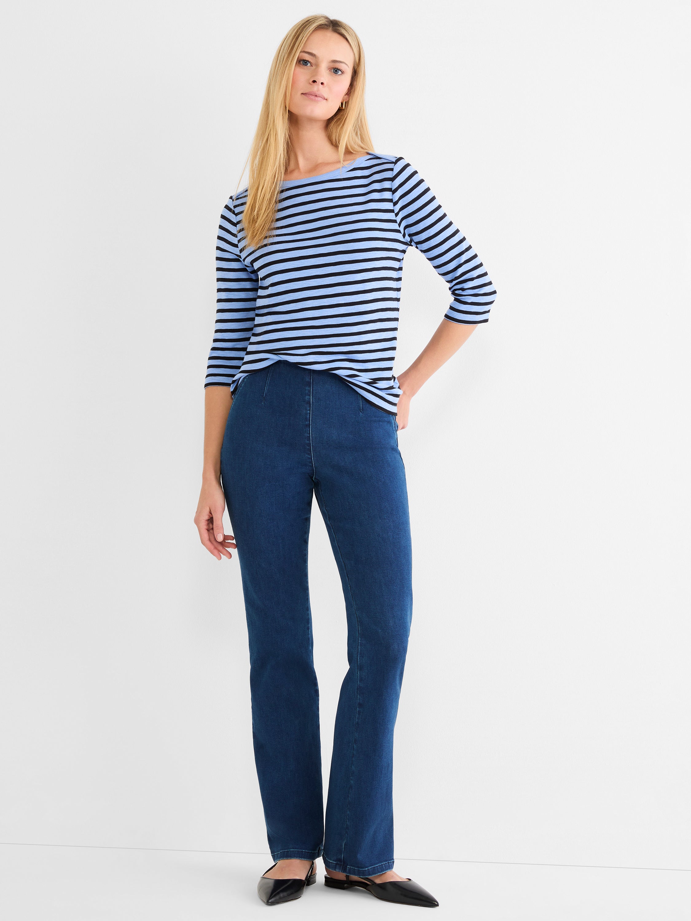 A fitted blue and black striped 3/4-sleeve top is paired with high-waisted, dark wash bootcut jeans.