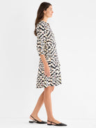 A model wears a short black and cream abstract print shirtdress with three-quarter sleeves and a flared skirt.