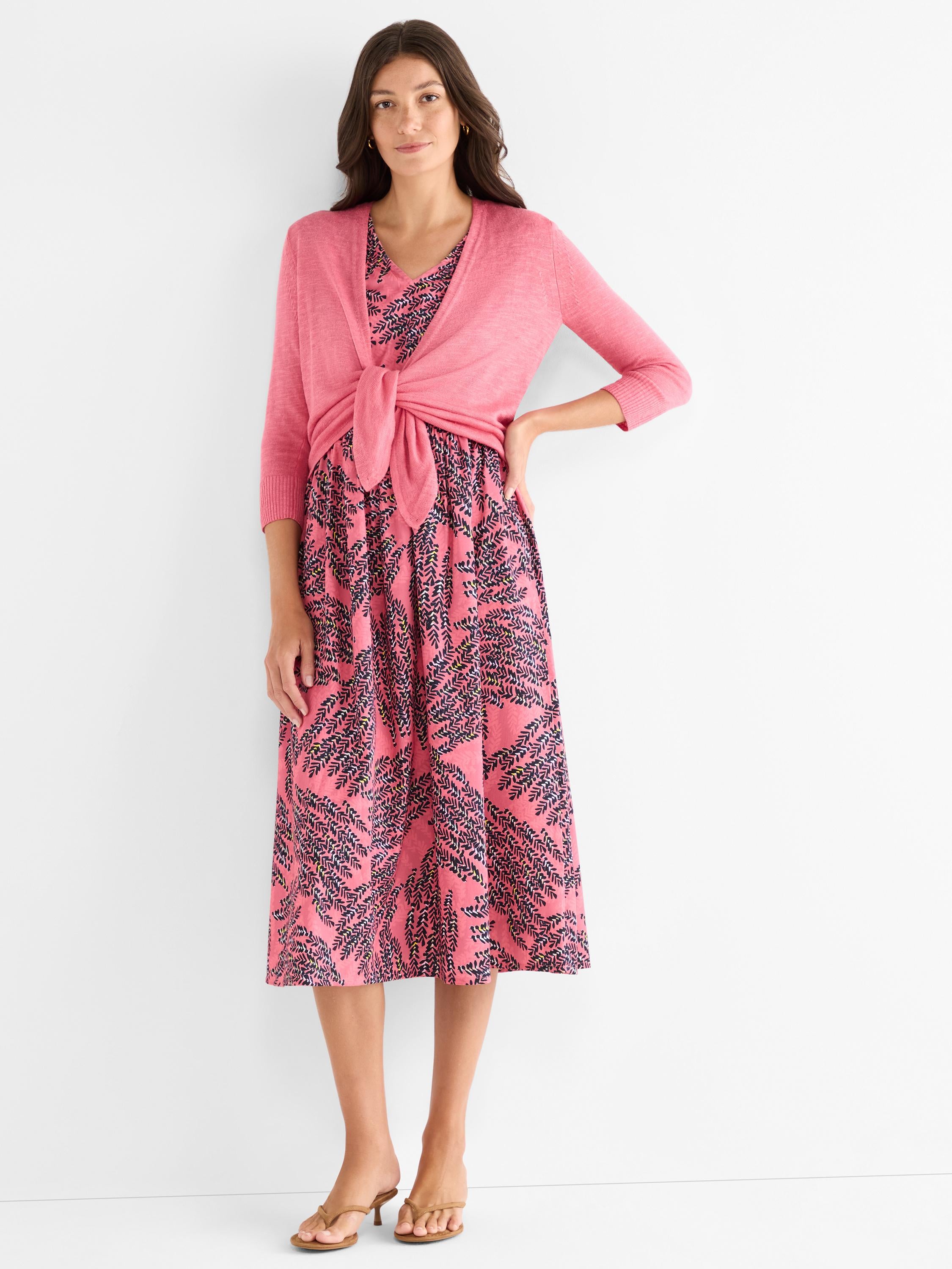 A pink abstract leaf print midi dress is layered with a solid pink knit cardigan tied in a knot at the front.