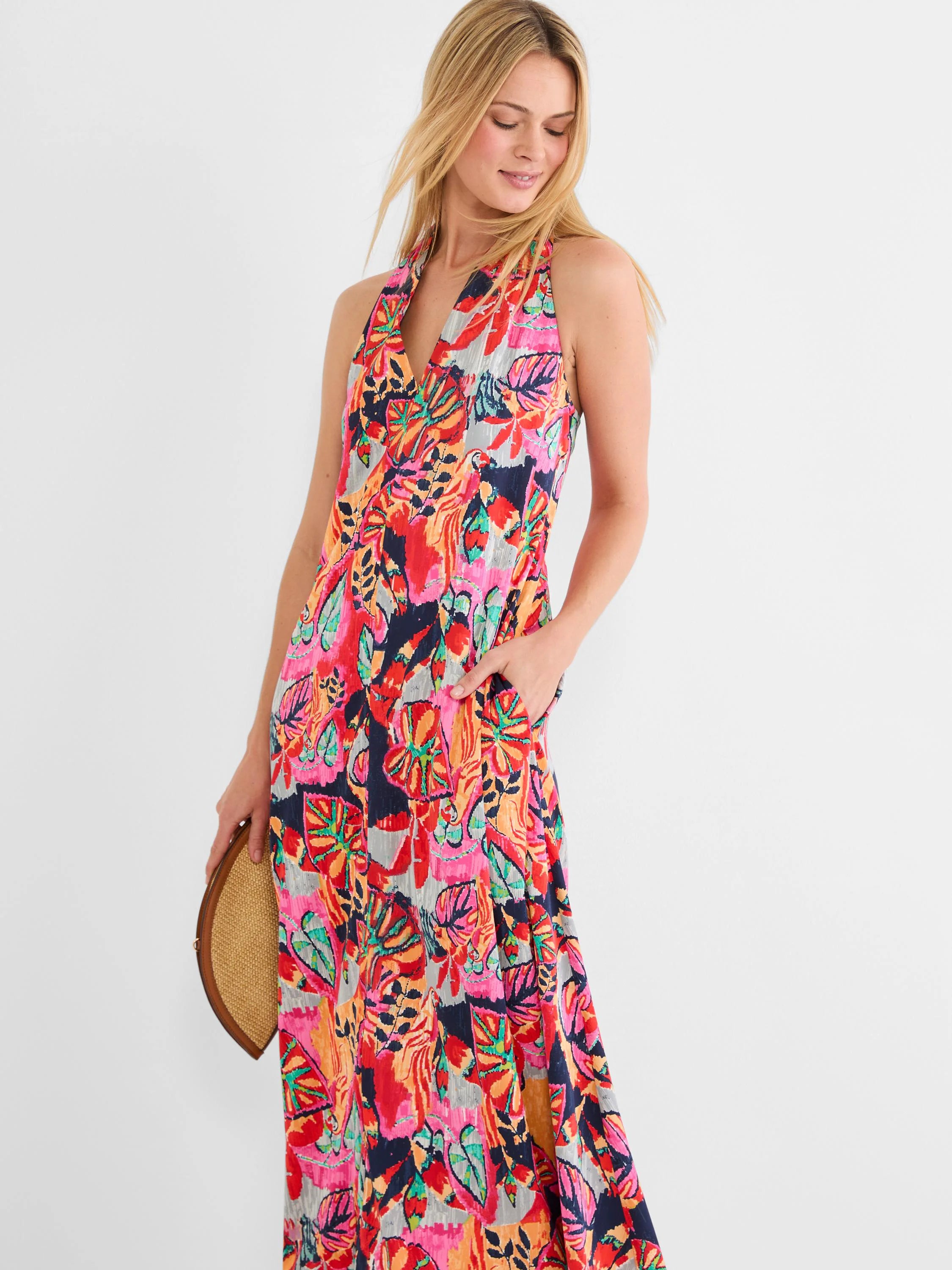 Halter V-neck maxi dress with a colorful tropical leaf print in pink, red, orange, teal, navy, and grey. Pockets visible.