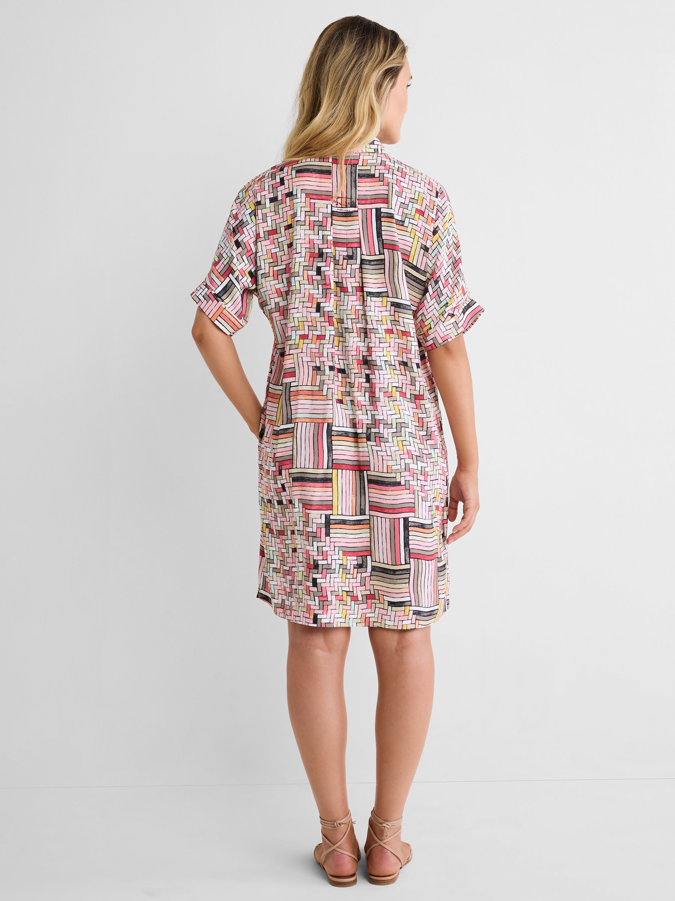 This relaxed shirt dress features a pink geometric grid print, short sleeves, and a straight knee-length fit.