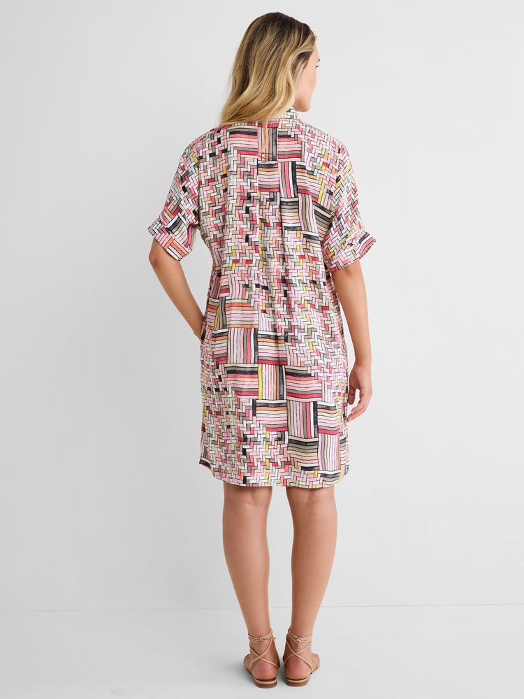 This relaxed shirt dress features a pink geometric grid print, short sleeves, and a straight knee-length fit.