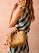 Tan woven straw bag with integrated handles and natural texture, styled with a peach patterned scarf.