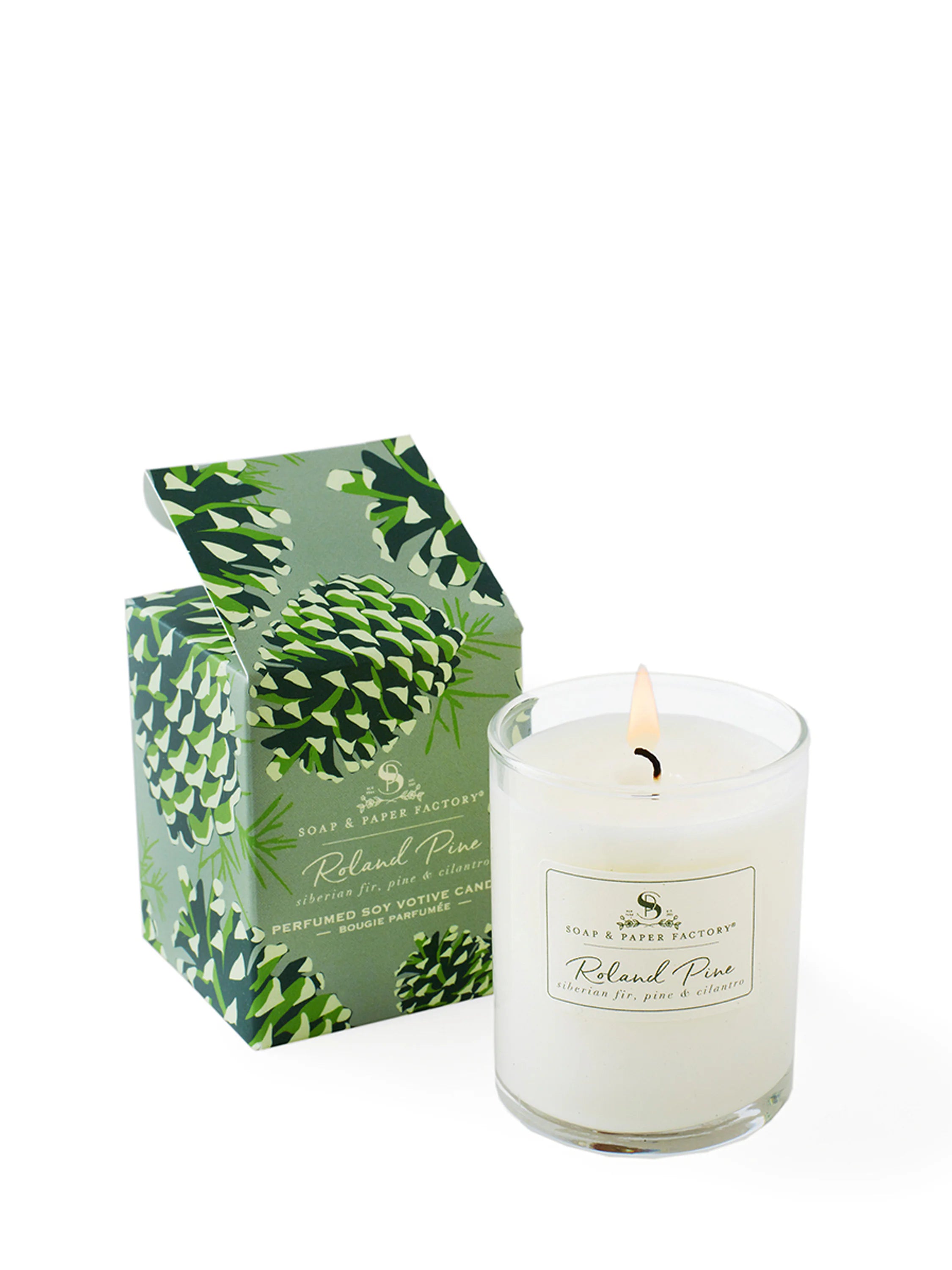 Off-white candle in clear glass is lit. Beside it is a sage green box with dark green pinecones, top flap open.