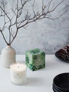Soy candle in clear glass, white wax, green/gray box with pine cone design.
