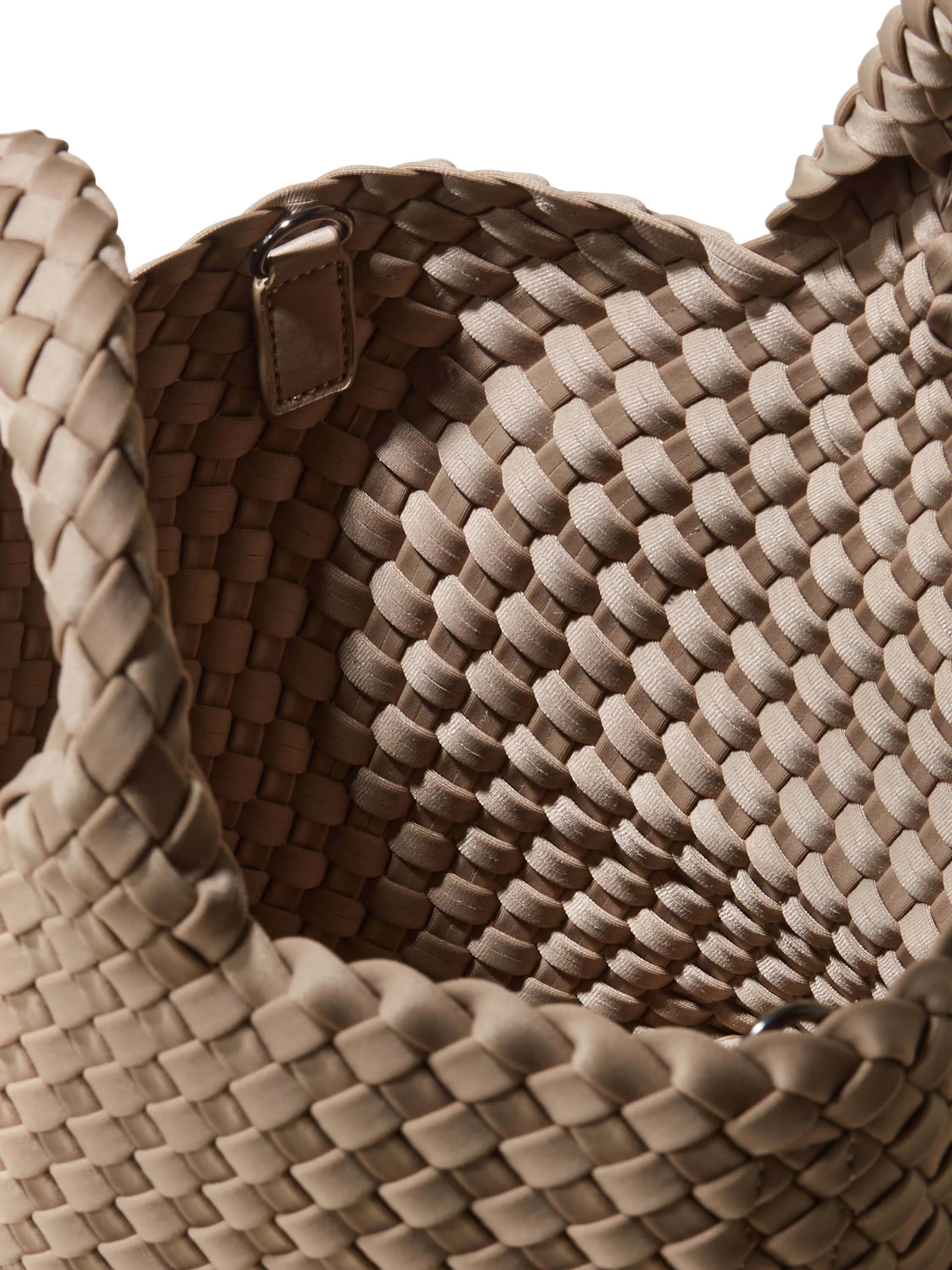 Close-up of a beige woven tote bag. It has a basket-like texture from intertwined fabric strips, with a small metal ring...