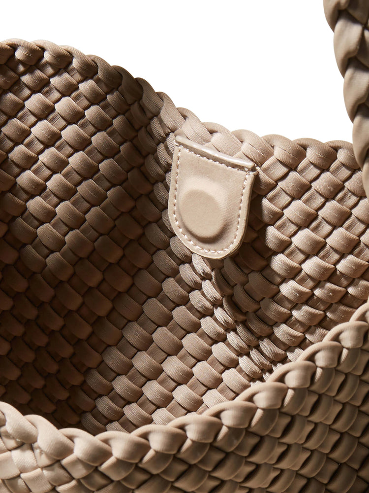 Tan hobo bag interior close-up, featuring a distinct woven pattern. A small, rounded beige closure tab with visible...