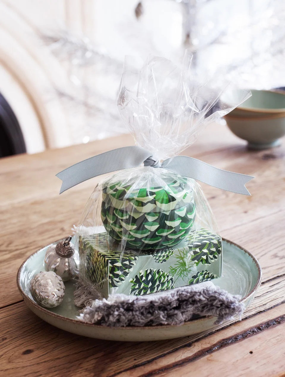 Green patterned candle and soap set, gift-wrapped in clear plastic with a light blue ribbon, on a pale green plate.