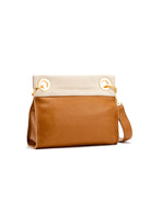 Tan pebbled leather crossbody bag with a cream top flap, featuring two gold-colored grommets and rings.