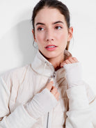 Ecru quilted jacket with smooth sleeves, high collar, silver zipper, and thumbhole cuffs.