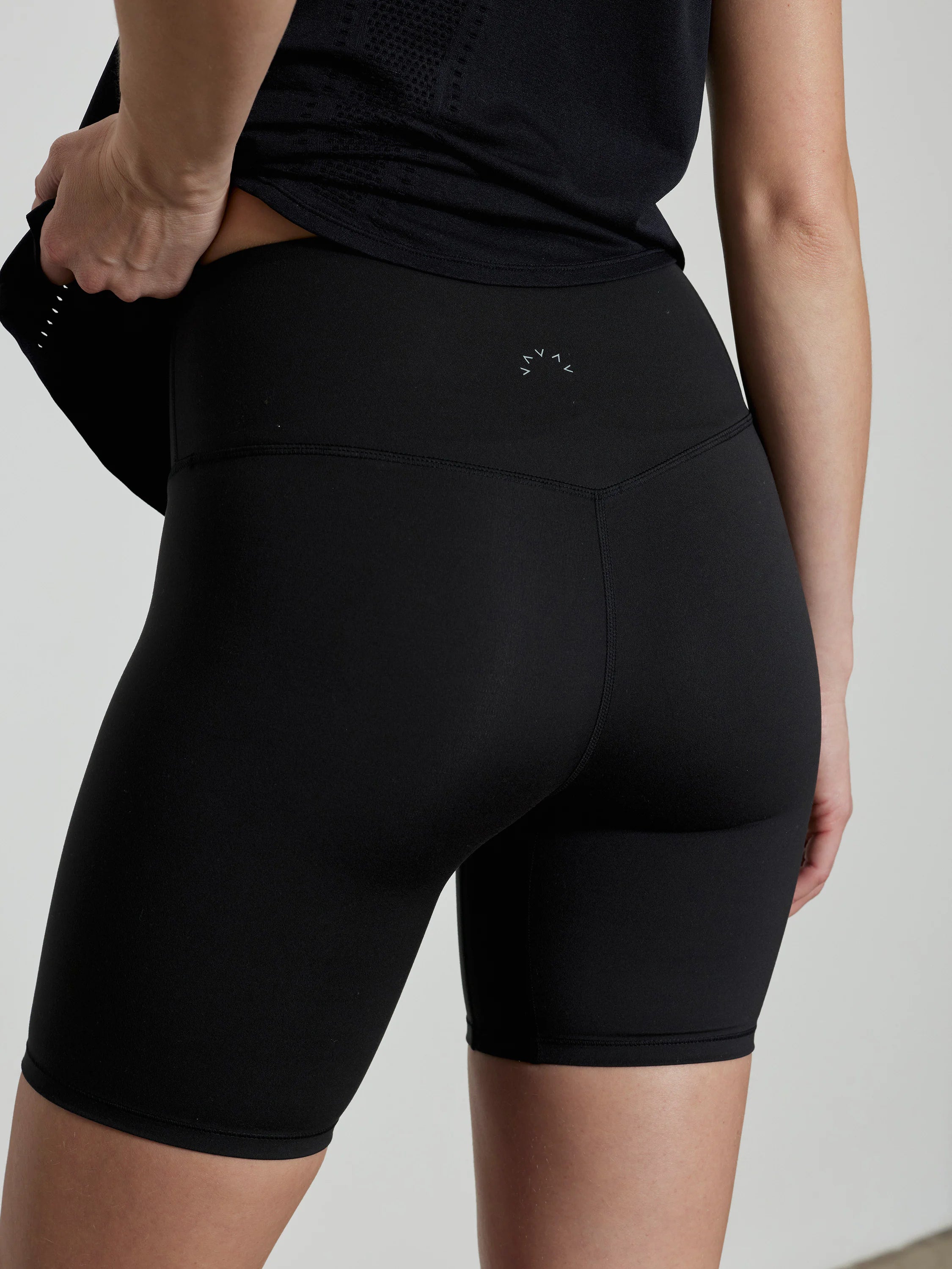 Black, high-waisted athletic shorts, mid-thigh length, with a subtle light grey logo on the back waistband.