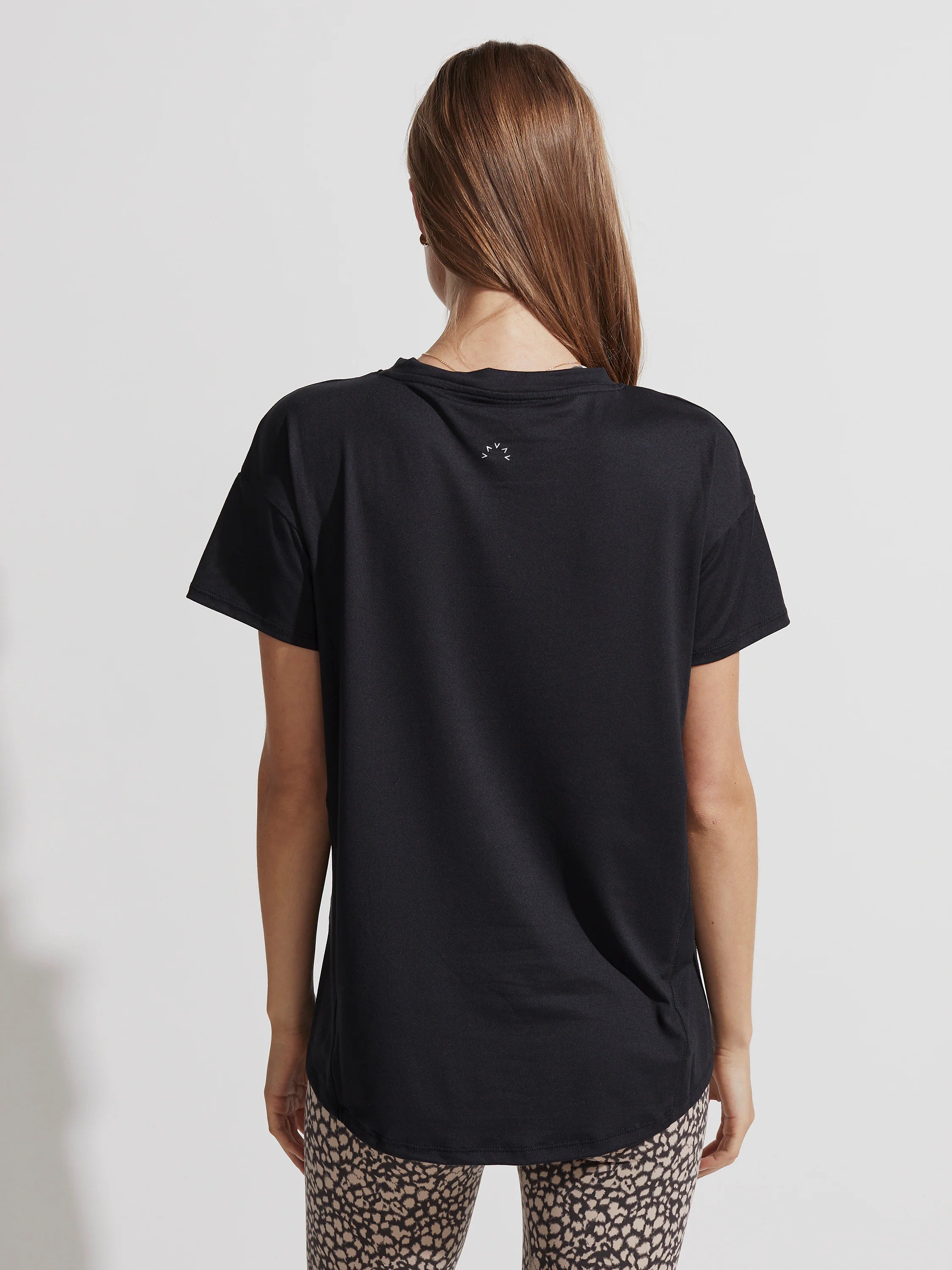Black, relaxed fit t-shirt with short sleeves and a crew neck, shown from the back. White logo on upper back, curved hem.