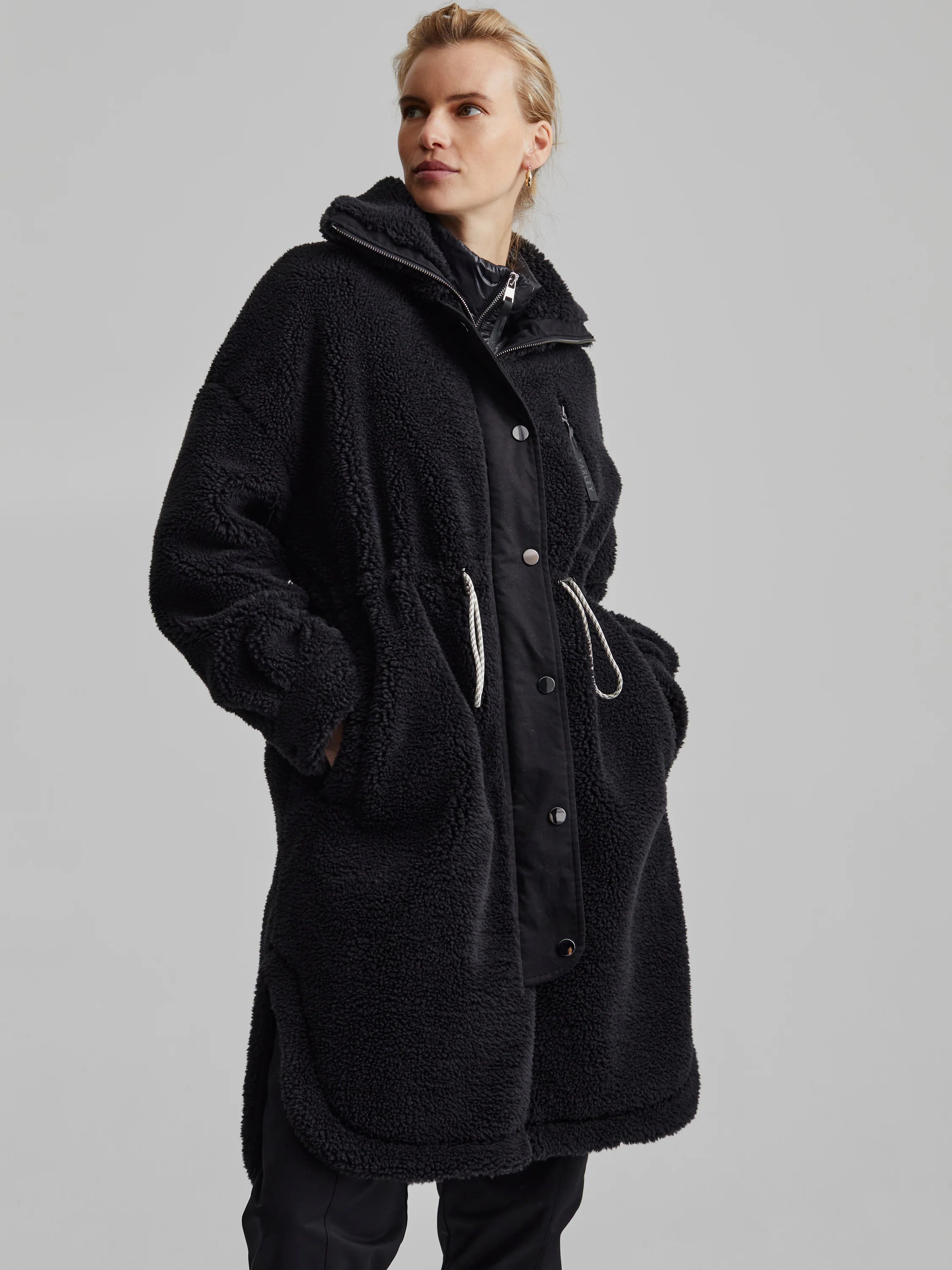 Black hooded longline sherpa coat with smooth center panel, dark buttons, zipper, and white drawstring details.