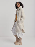 Cream midi-length sherpa coat with a high collar, full zipper, and drawstring waist.
