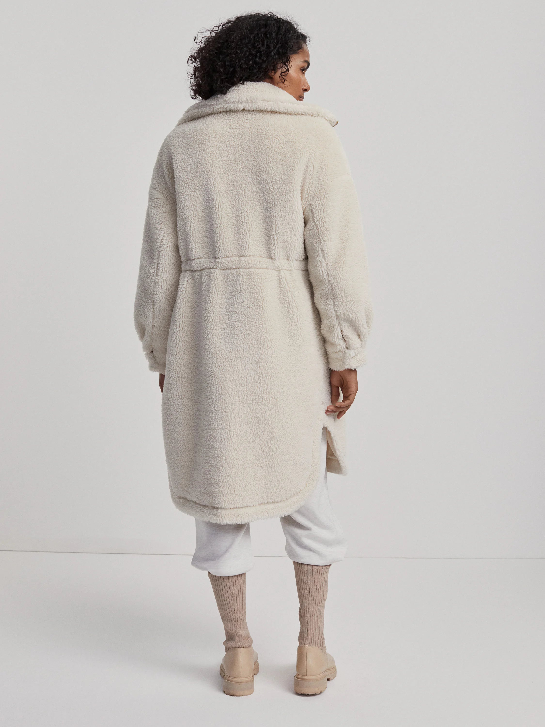 Cream teddy fleece coat with wide collar, cinched waist, long sleeves, and rounded hem with side slits.