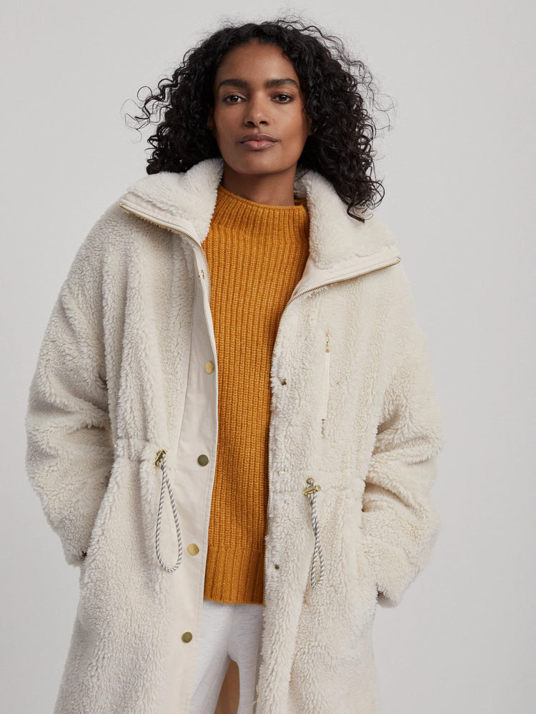 Cream sherpa fleece coat with a high collar, full-zip, and drawstring waist, featuring gold hardware.