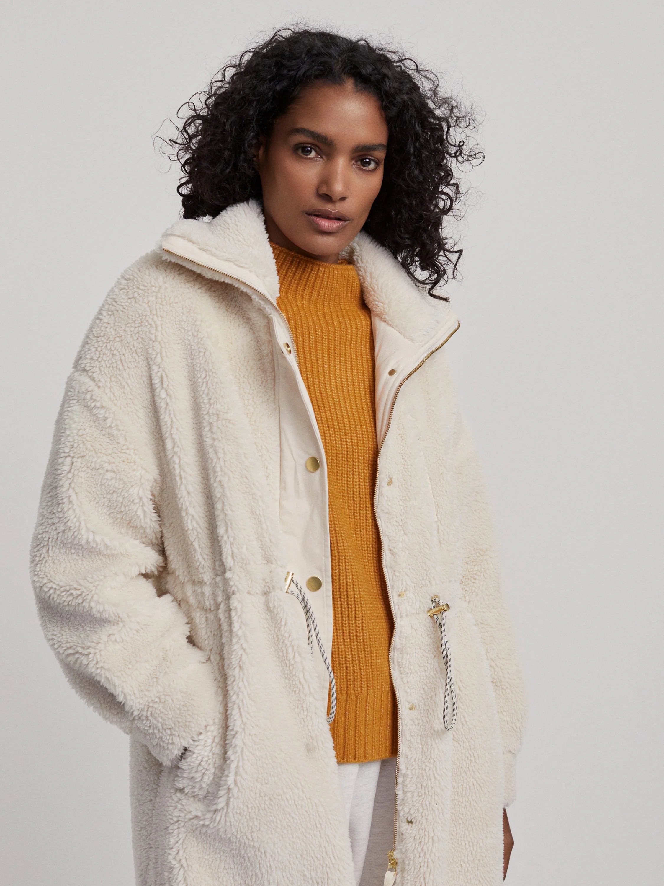 Off-white long teddy-style coat with gold zipper and drawstring.  Features a contrasting off-white inner layer.