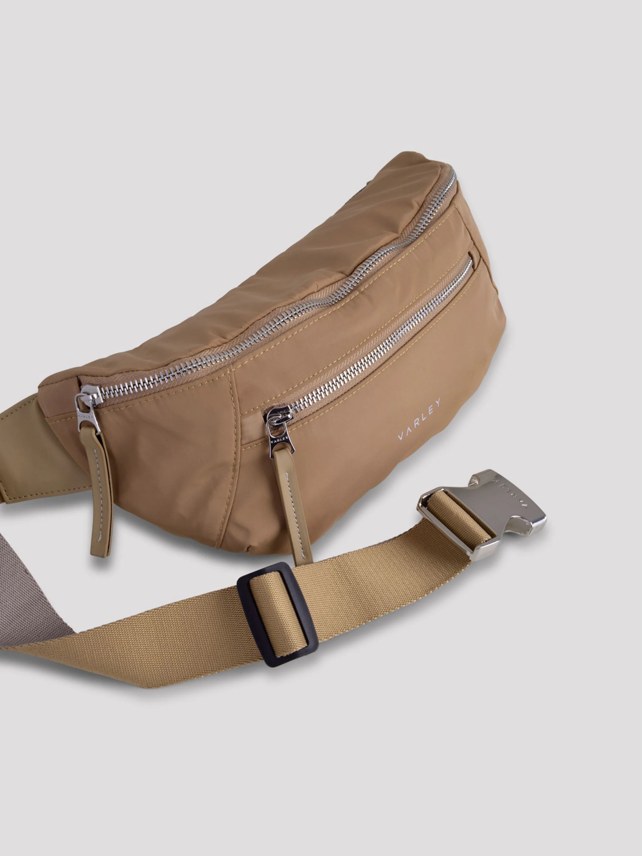 Beige curved belt bag with silver zippers and buckle.  Tan adjustable strap with black slider.