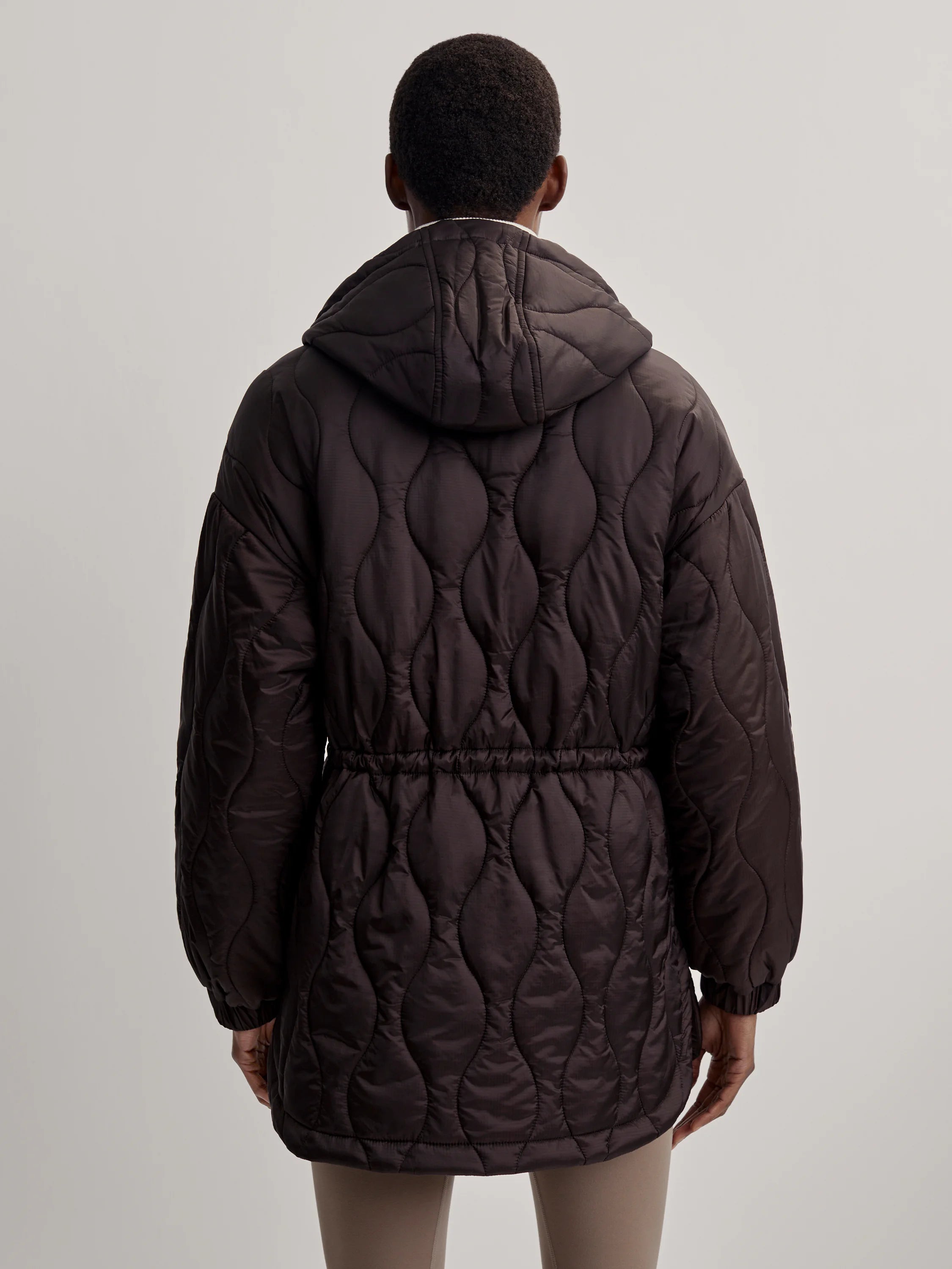 Dark brown hooded quilt jacket with wavy pattern and cinched drawstring waist, seen from back.