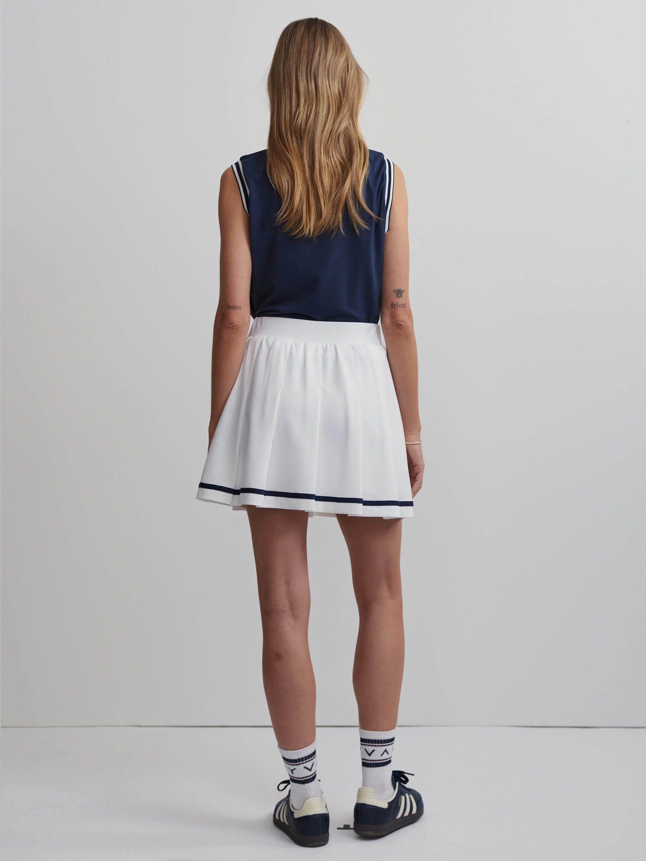 White pleated skort with navy blue trim; model wears navy top and white socks.