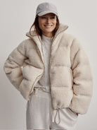 Off-white sherpa jacket with gold zipper.  Puffy design. Model also wears light grey cap and pants.