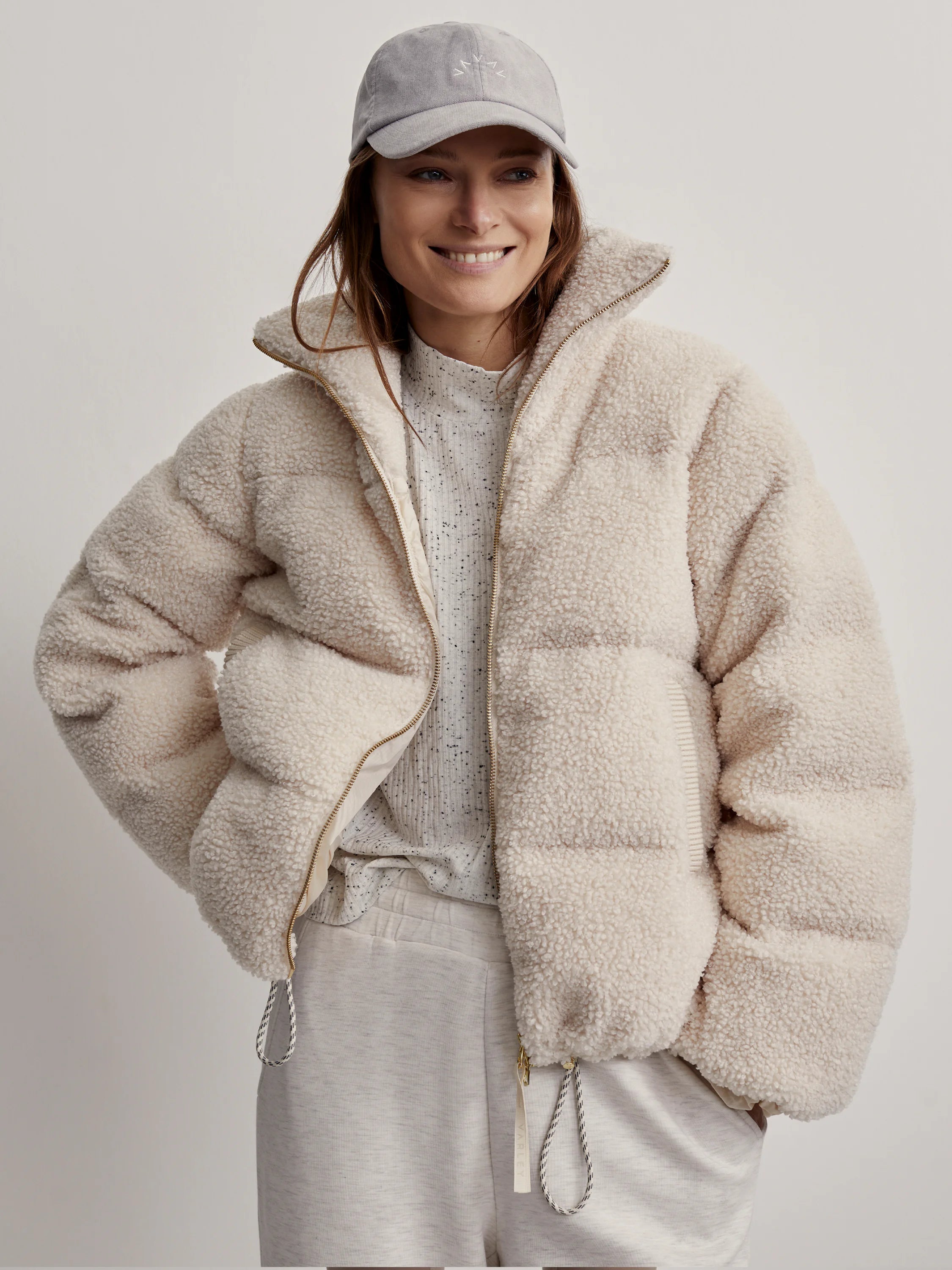 Cream sherpa puffer jacket with a high collar, gold zipper, and hem drawstrings.