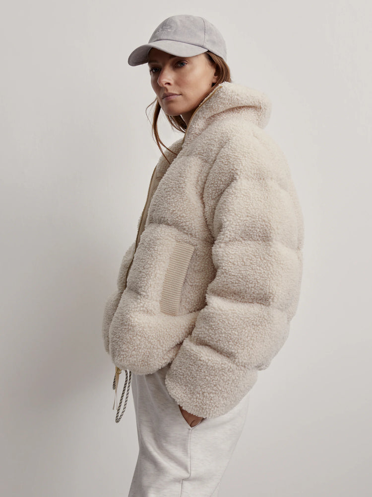 Off-white sherpa jacket with a gold zipper and beige ribbed details.  The jacket is puffy and has a textured surface.