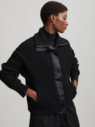Black ribbed knit mock neck sweater with silver front zipper, smooth satin panels, and gathered sleeves.