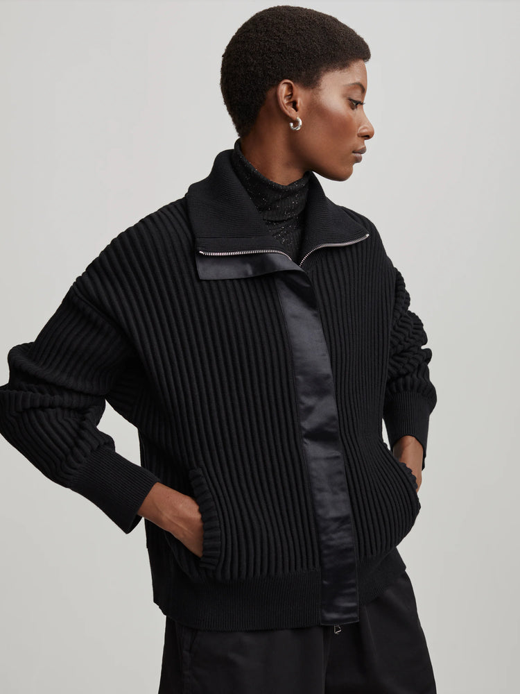 Black ribbed knit mock neck sweater with silver front zipper, smooth satin panels, and gathered sleeves.